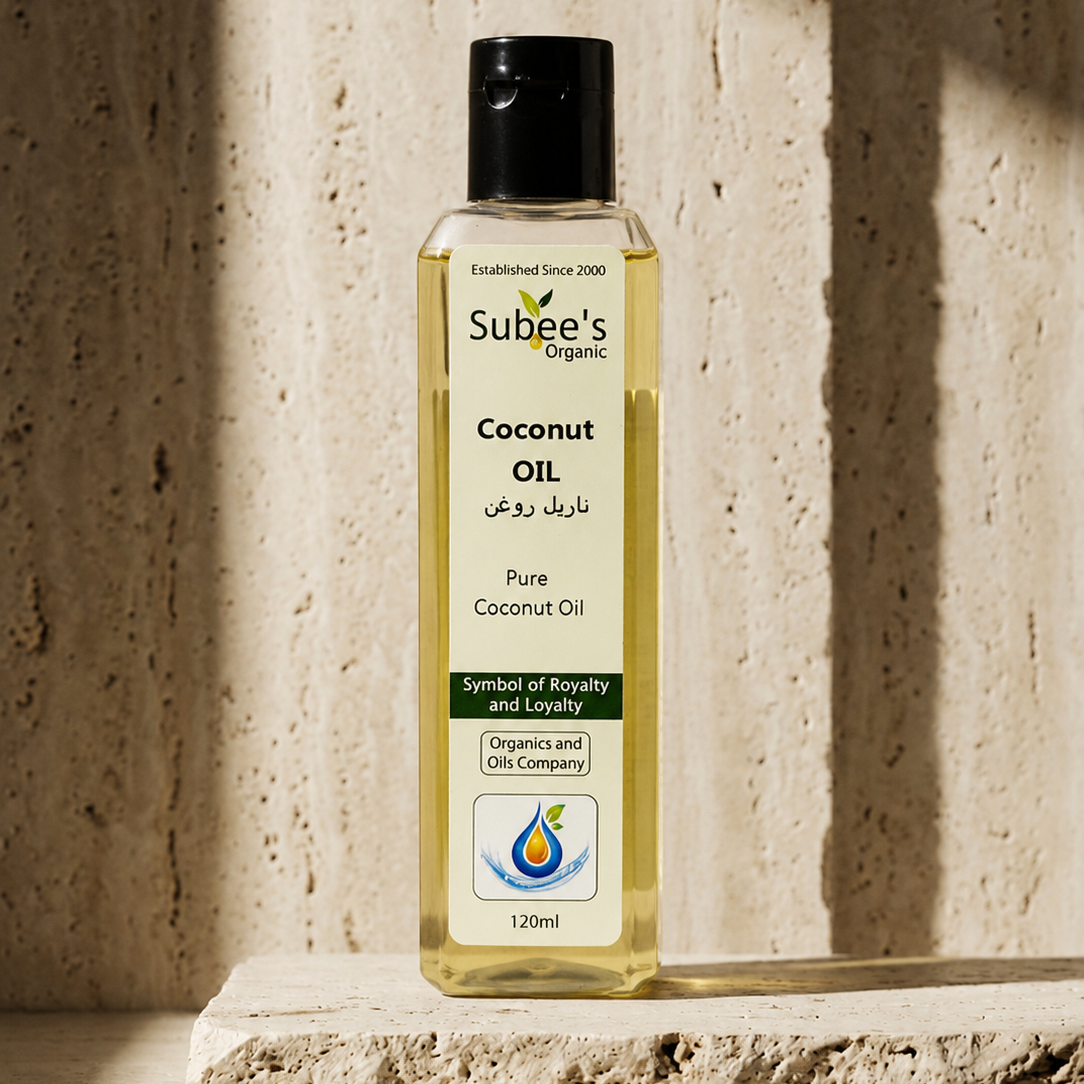 A bottle of Subee's Organic Coconut Oil stands on a textured stone slab against a matching stone wall, lit by warm directional sunlight with soft shadows.