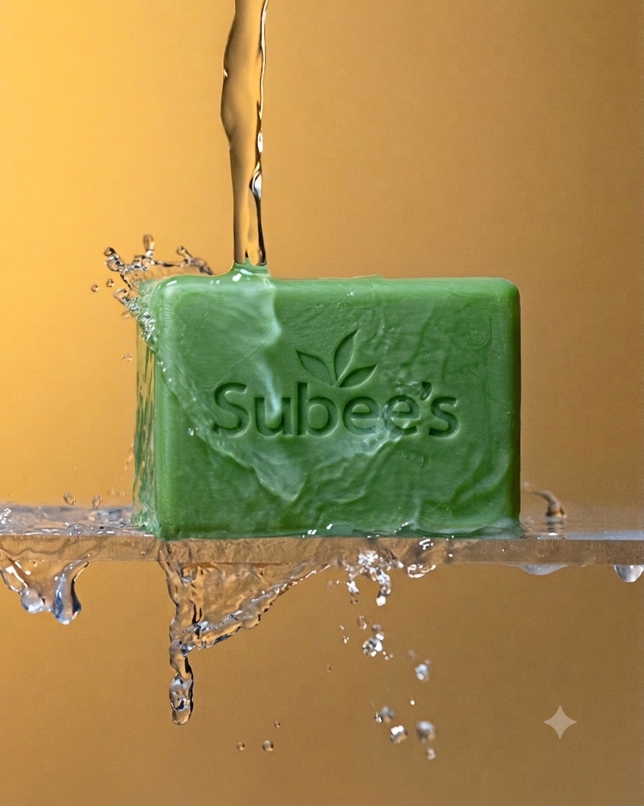 A green rectangular bar of Subbee's soap with a leaf logo, partially submerged in splashing water against a warm golden-brown background.
