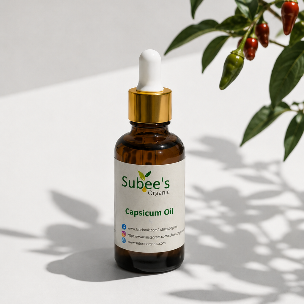 A bottle of Subee's Organic Capsicum Oil with a white dropper cap and gold collar, set on a white surface with leafy plant shadows. The product label clearly shows the brand 'Subee's Organic' and the product name 'Capsicum Oil'.