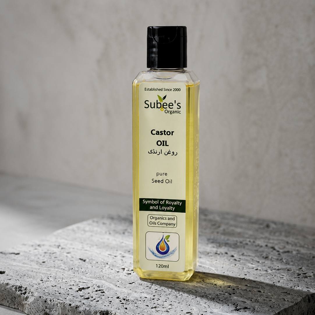 A bottle of Subee's Organic Castor Oil (Rouge Arkik) standing on a textured gray stone slab against a neutral gray concrete wall background.