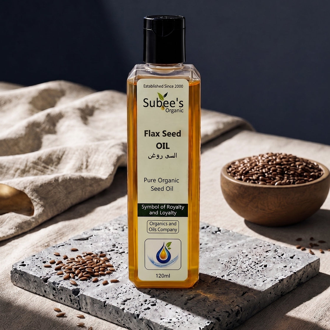 A bottle of Subee's Organic Flax Seed Oil stands on a stone slab in a styled studio setup with linen cloth, scattered flax seeds, and a small bowl of flax seeds.