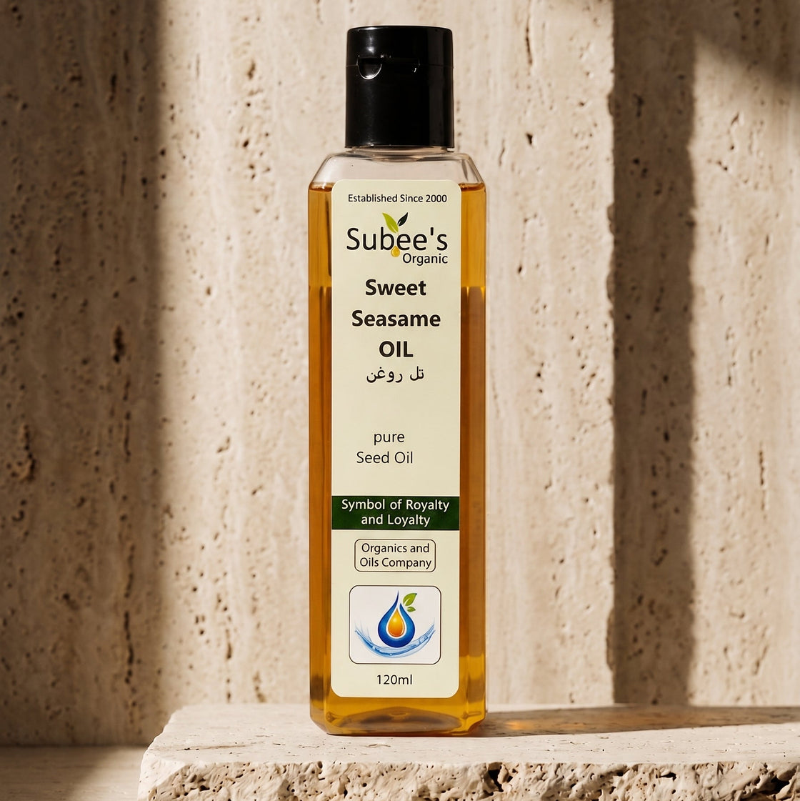A bottle of Subee's Organic Sweet Seameste Oil (pure seed oil) standing on a textured stone slab against a matching stone wall with dramatic diagonal shadows.
